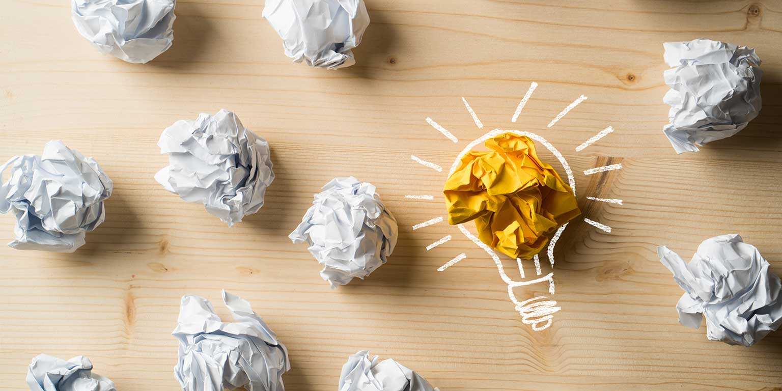 Photograph of crumpled balls of paper with one yellow crumpled ball of paper outlined with a drawing of a light bulb