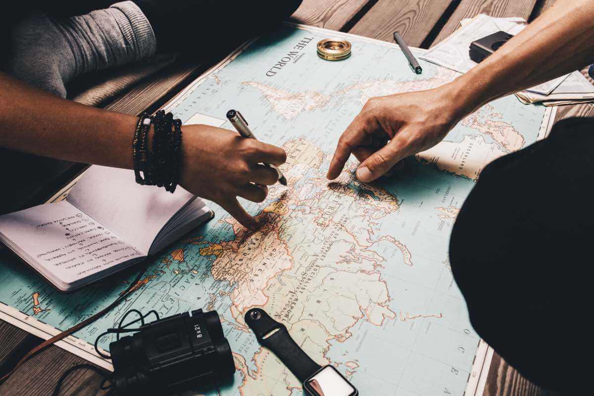 Photograph of two people's hands pointing and drawing on a world map
