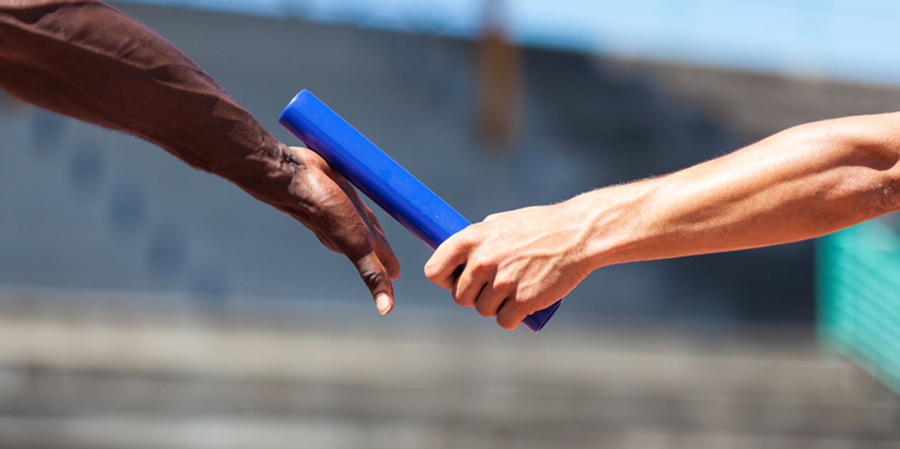 Photograph of one athlete's hand passing a baton to another athlete's hand