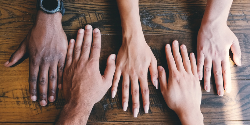 Photograph of five hands lined up side-by-side on a wood table