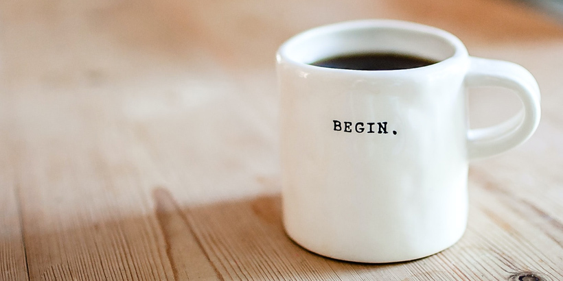 Photograph of cup of coffee with the word begin on the mug
