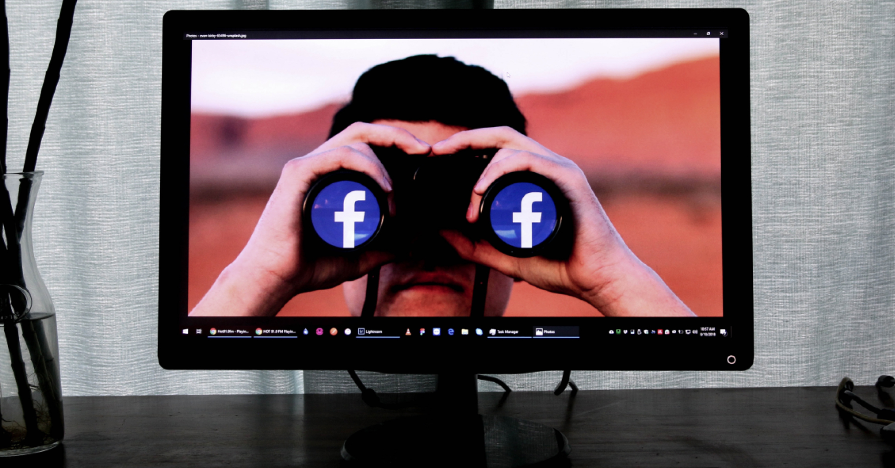 Computer monitor with a person holding binoculars that have the Facebook logo