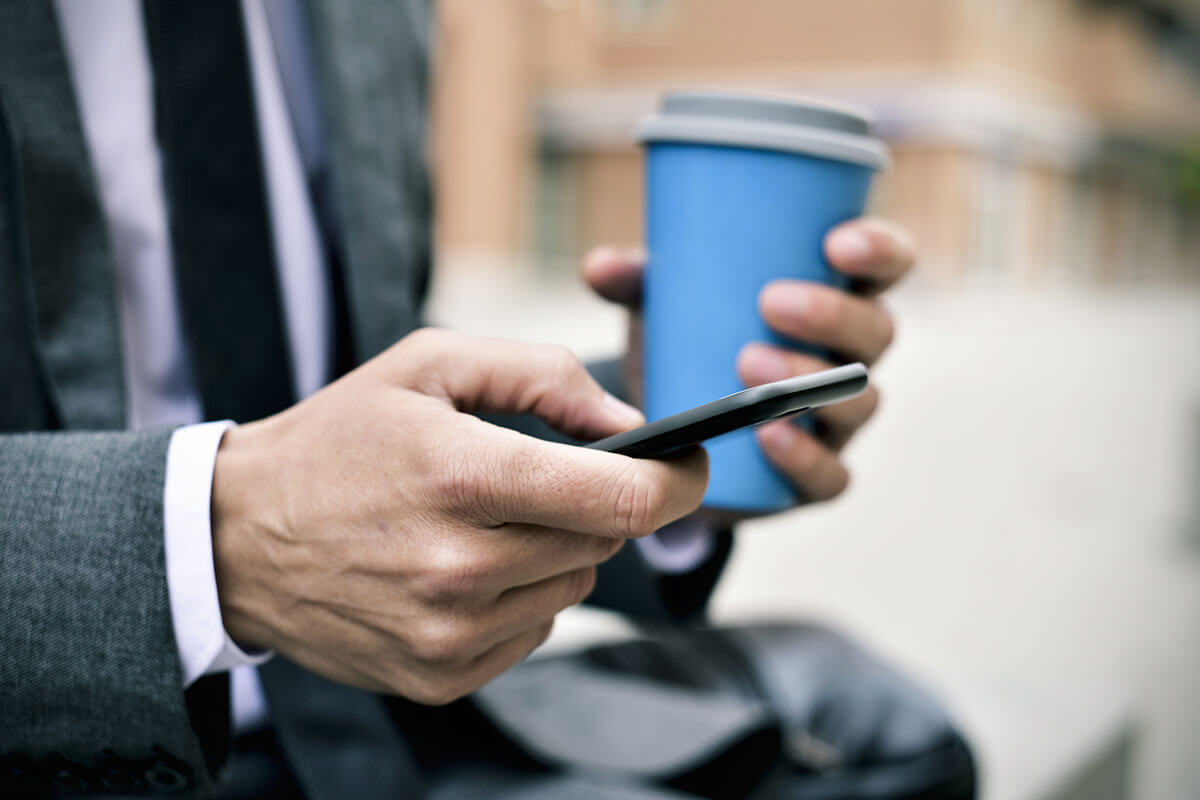 Photograph of a sales rep's hands holding coffee and a smartphone