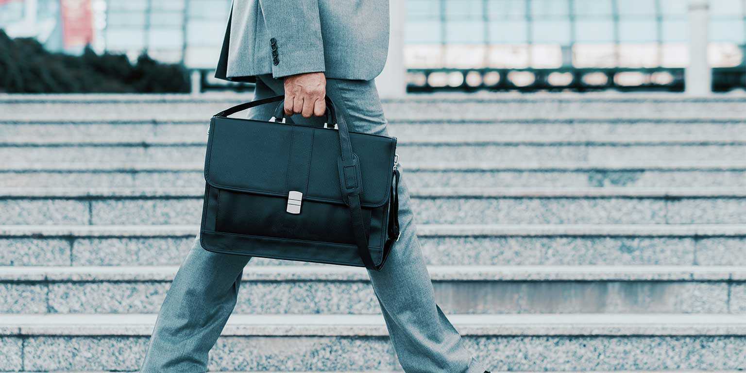 Photograph of a sales rep wearing a suit walking with a black briefcase