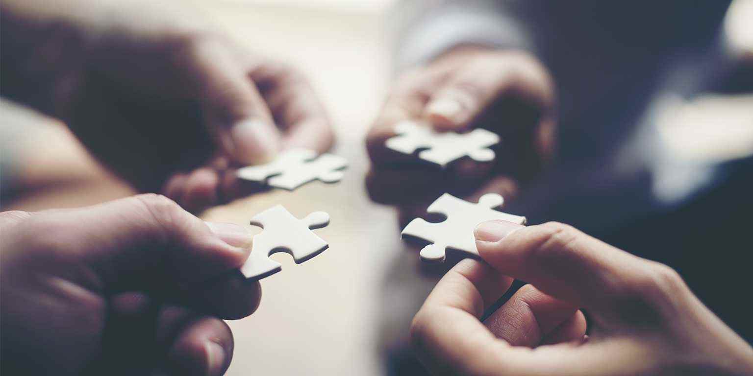 Photograph of four hands in a circle holding puzzle pieces