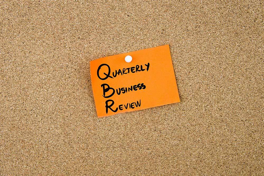 Photograph of an orange note that says Quarterly Business Review pinned to a cork board