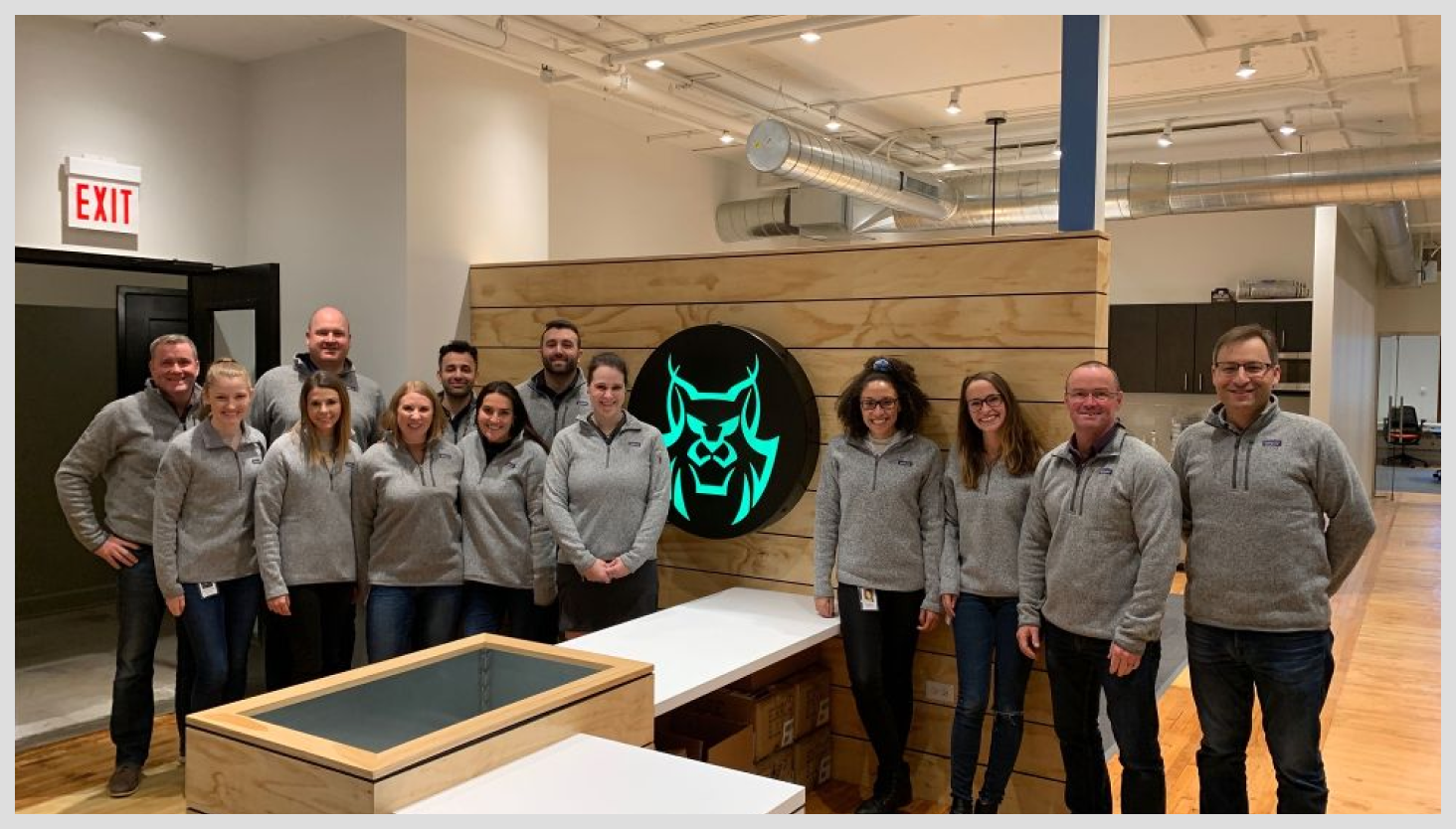 AccuLynx employees in front of logo wearing the matching grey sweaters