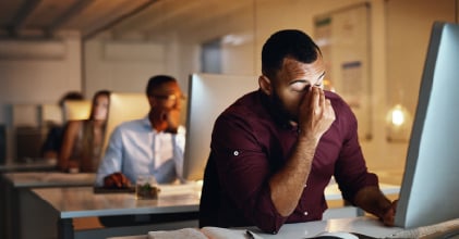 Photograph of sales rep rubbing their eyes in front of a computer in an office