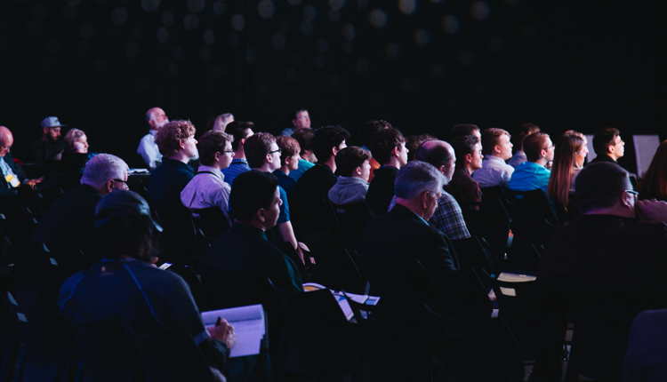 Photograph of a crowd of conference attendees seated in a dark auditorium