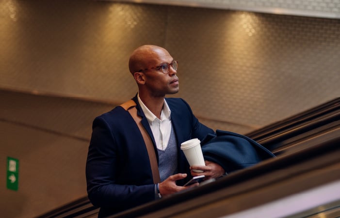 Photograph of a finance leader holding a mobile phone and riding up an escalator
