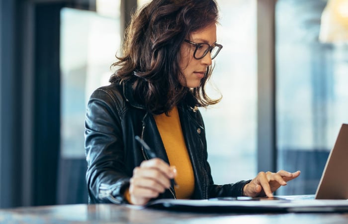 Photograph of a marketing leader writing notes and typing on a laptop