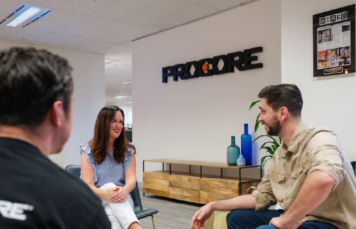 Photograph of three Procore employees talking in the office