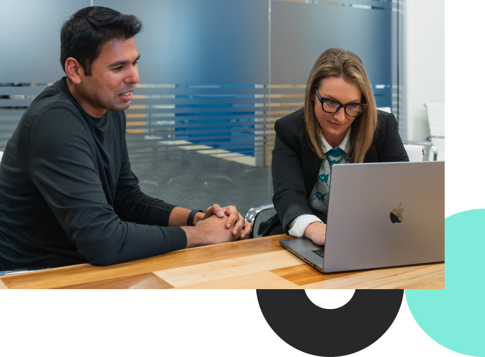 Photograph of two revenue professionals sitting at a conference table, one typing on a laptop